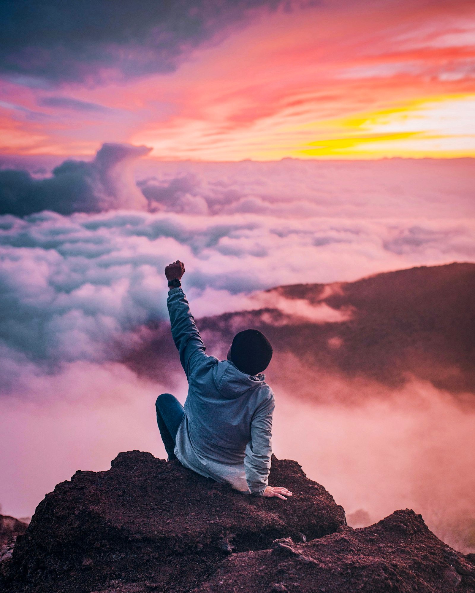 A person on a mountain cliff raising a hand in triumph at golden hour, symbolizing achievement